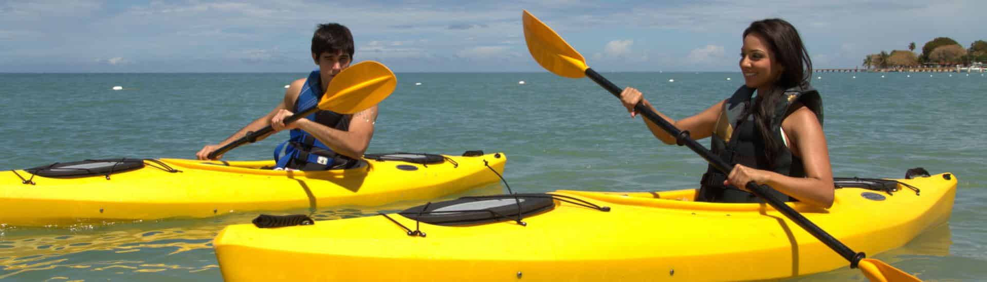 Two people on two yellow kayaks floating on blueish green water