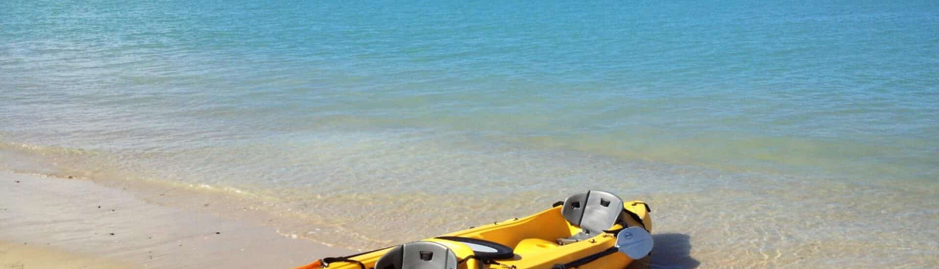 Kayak amarillo en la playa de arena blanca con agua azul al fondo