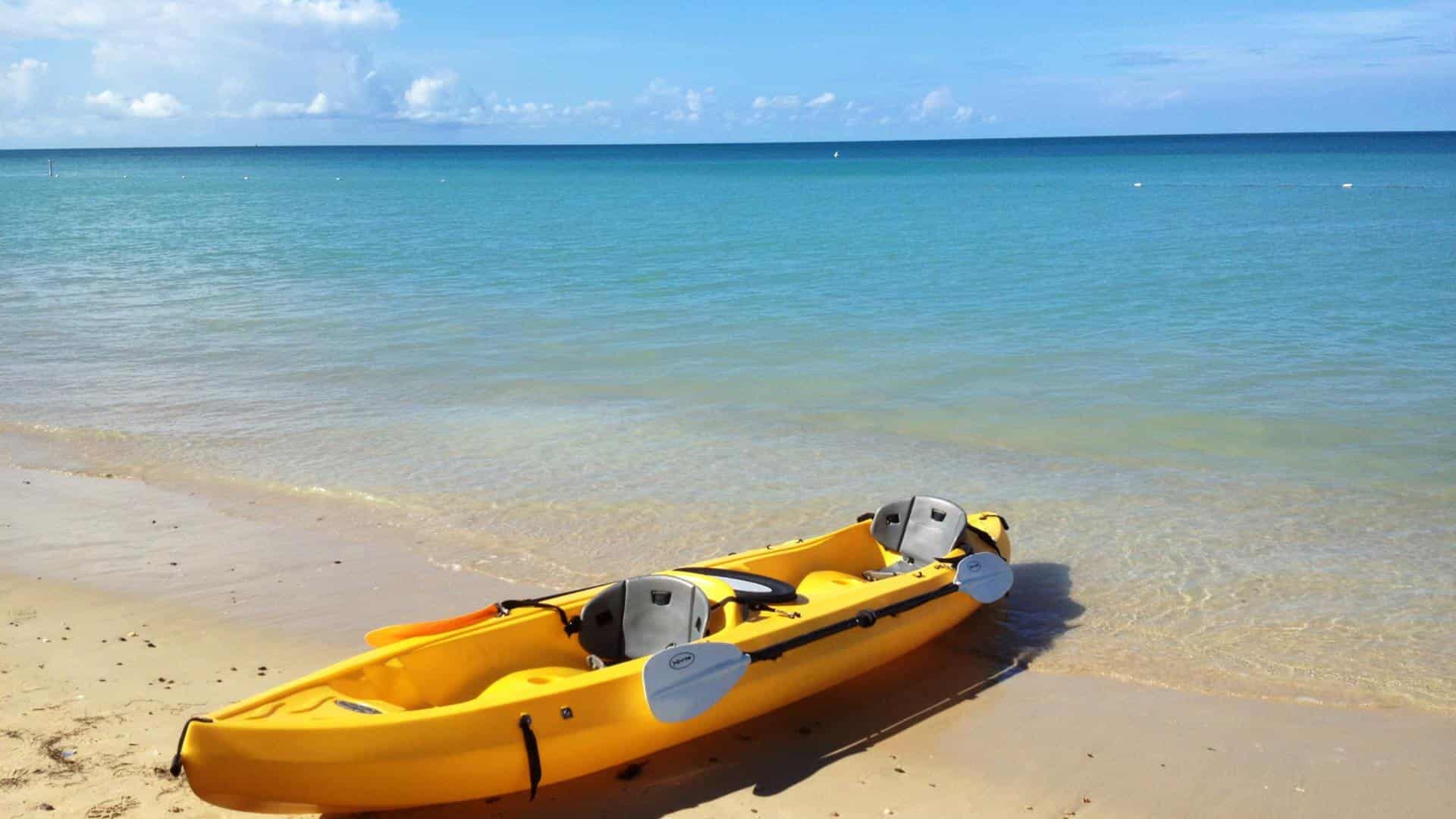 Yellow kayak on white sandy beach with blue water in the background