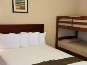 Suite with tan walls, tile flooring, dark wooden furniture, queen bed with white bedding, and bunk bed with tan bedding