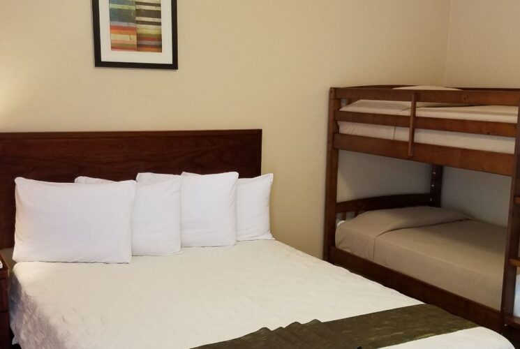 Suite with tan walls, tile flooring, dark wooden furniture, queen bed with white bedding, and bunk bed with tan bedding