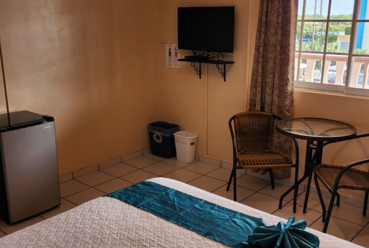 Bedroom with tan walls, tile flooring, white bedding, mini fridge, flat-screen TV, and sitting area