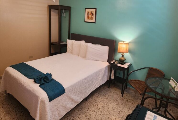 Bedroom with turquoise and tan walls, tile flooring, bed with white bedding, sitting area, and mini fridge