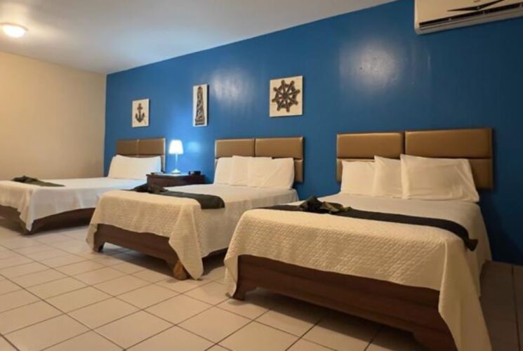 Bedroom with blue and tan walls, tile flooring, and three beds with white bedding