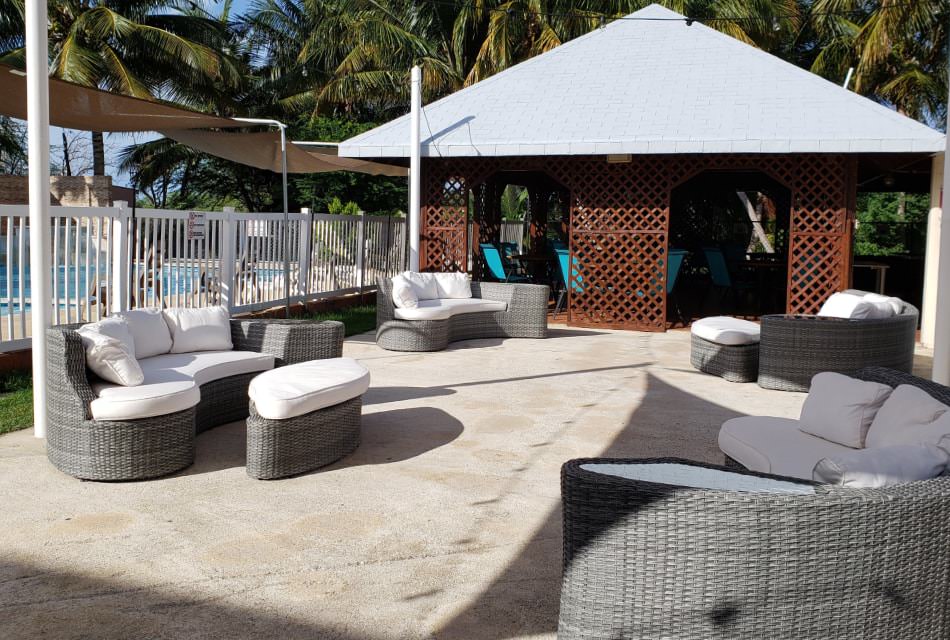 Concrete patio with multiple gray wicker sofas next to a pool and a covered outdoor pavilion with patio tables and chairs