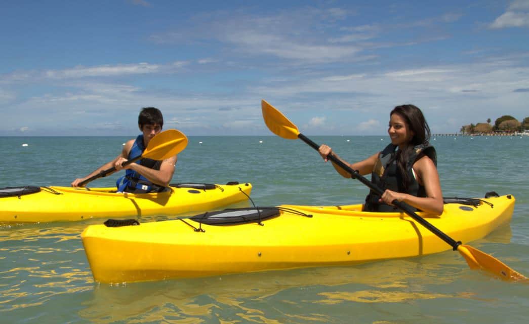 Two people in individual yellow kayaks paddling through blue-green water